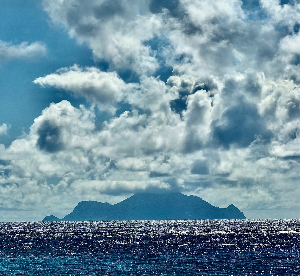The island of Saba silhouetted on the horizon under dramatic clouds.
