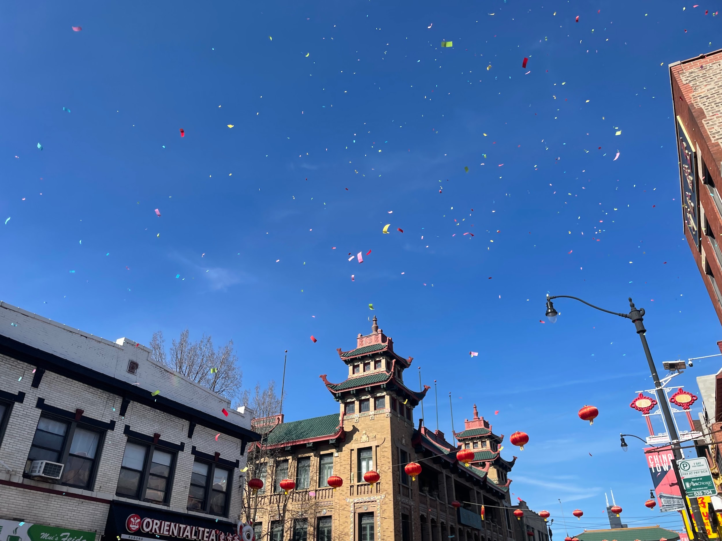 Red lanterns and confetti fill a clear blue sky over Chinatown buildings during the 2026 Lunar New Year Parade
