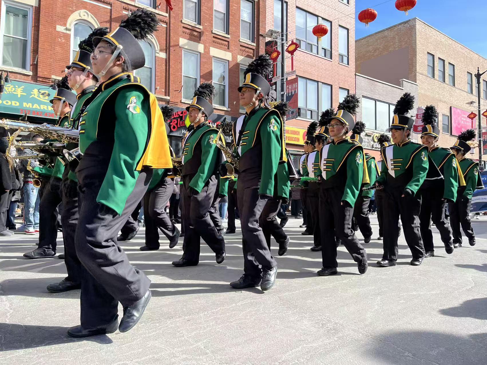 A school marching band in green and yellow uniforms marching through Chinatown in the Lunar New Year Parade