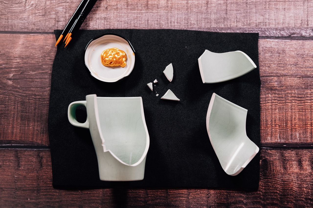 Broken celadon mug and plate pieces beside a dish of gold lacquer