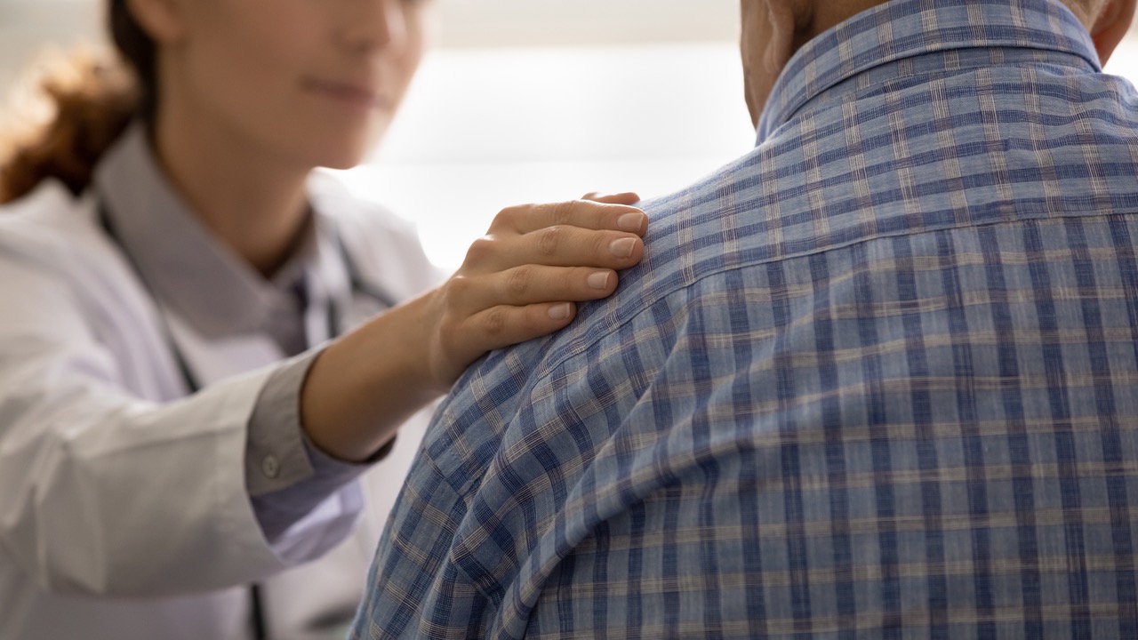 A caregiver's hand on an elderly patient's shoulder